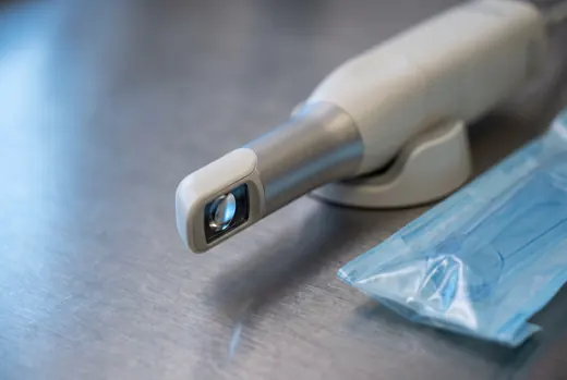 An intraoral digital scanning wand resting on a stainless bench beside its cradle